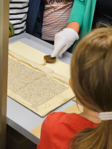 Kinder betrachten eine historische Urkunde mit Siegel, während eine Mitarbeiterin des Archivs einzelne Details erklärt.